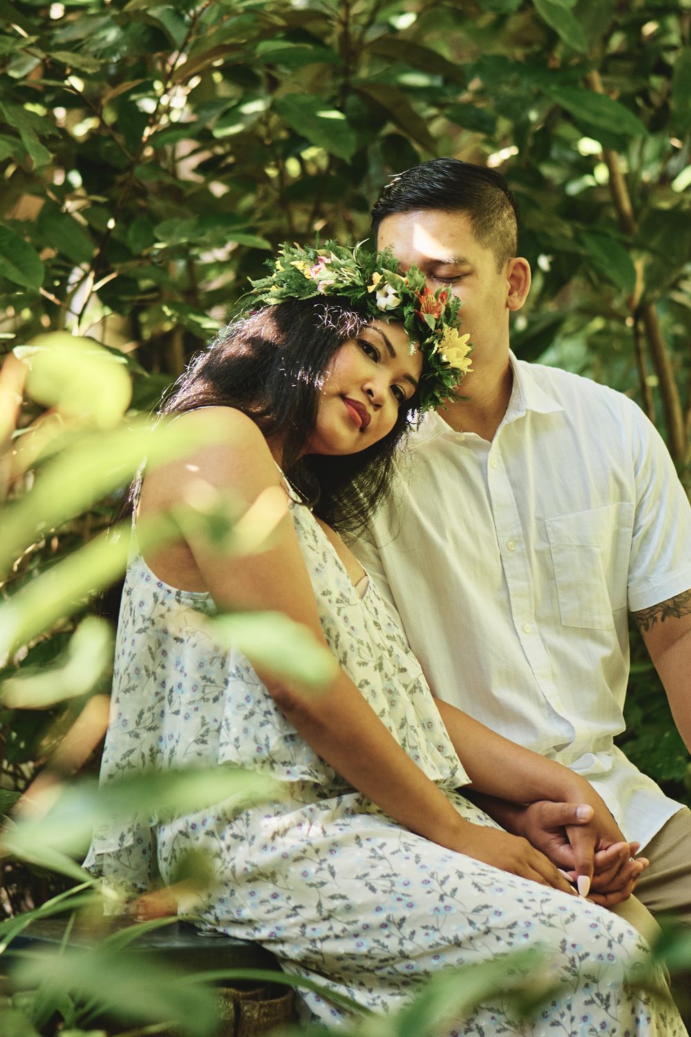 A couple relaxes together among green foliage in a garden setting.