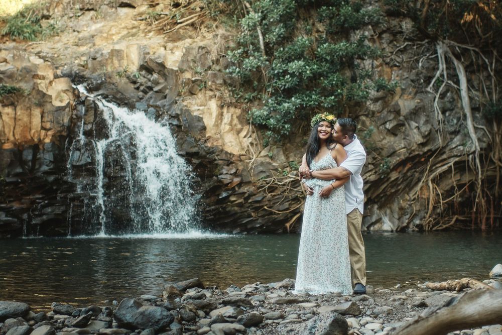 A romantic couple poses near a scenic waterfall in a tropical setting.