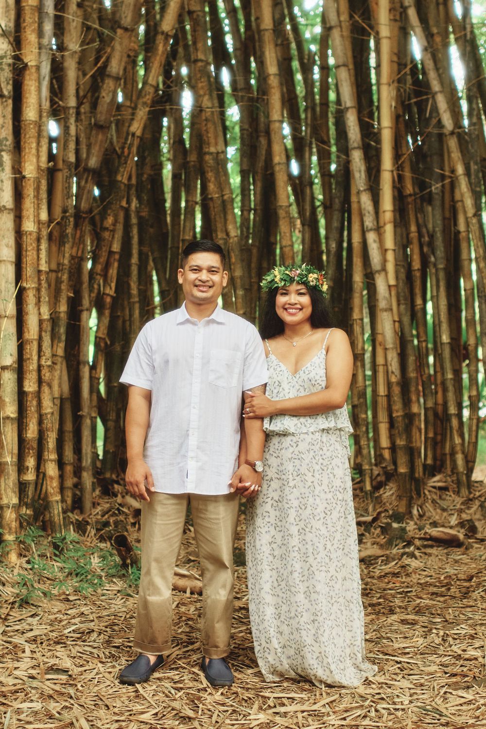 A couple stands together in a bamboo forest wearing coordinated white and beige outfits.