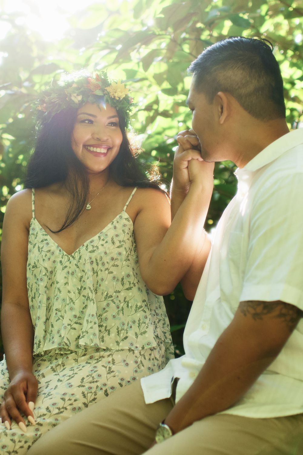 A sunlit engagement photo of a couple sharing a tender moment in a garden setting.