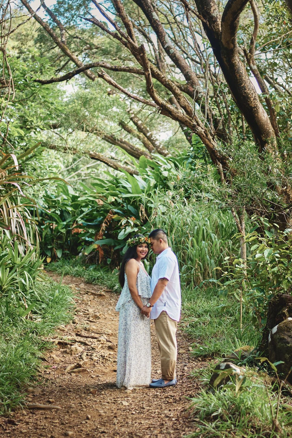 A couple walks hand in hand along a scenic forest trail surrounded by lush greenery.