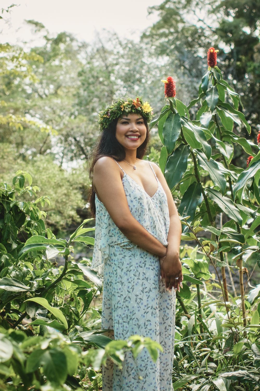 A person in a floral dress poses in a tropical garden wearing a flower crown.