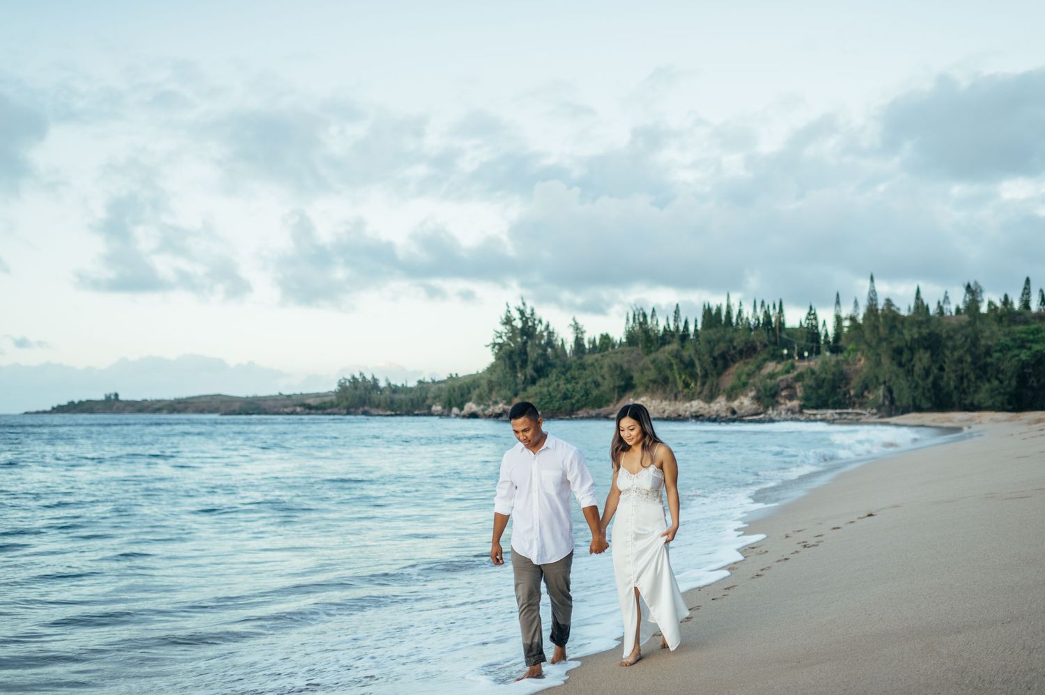 A couple walks hand in hand along a serene beach shoreline.