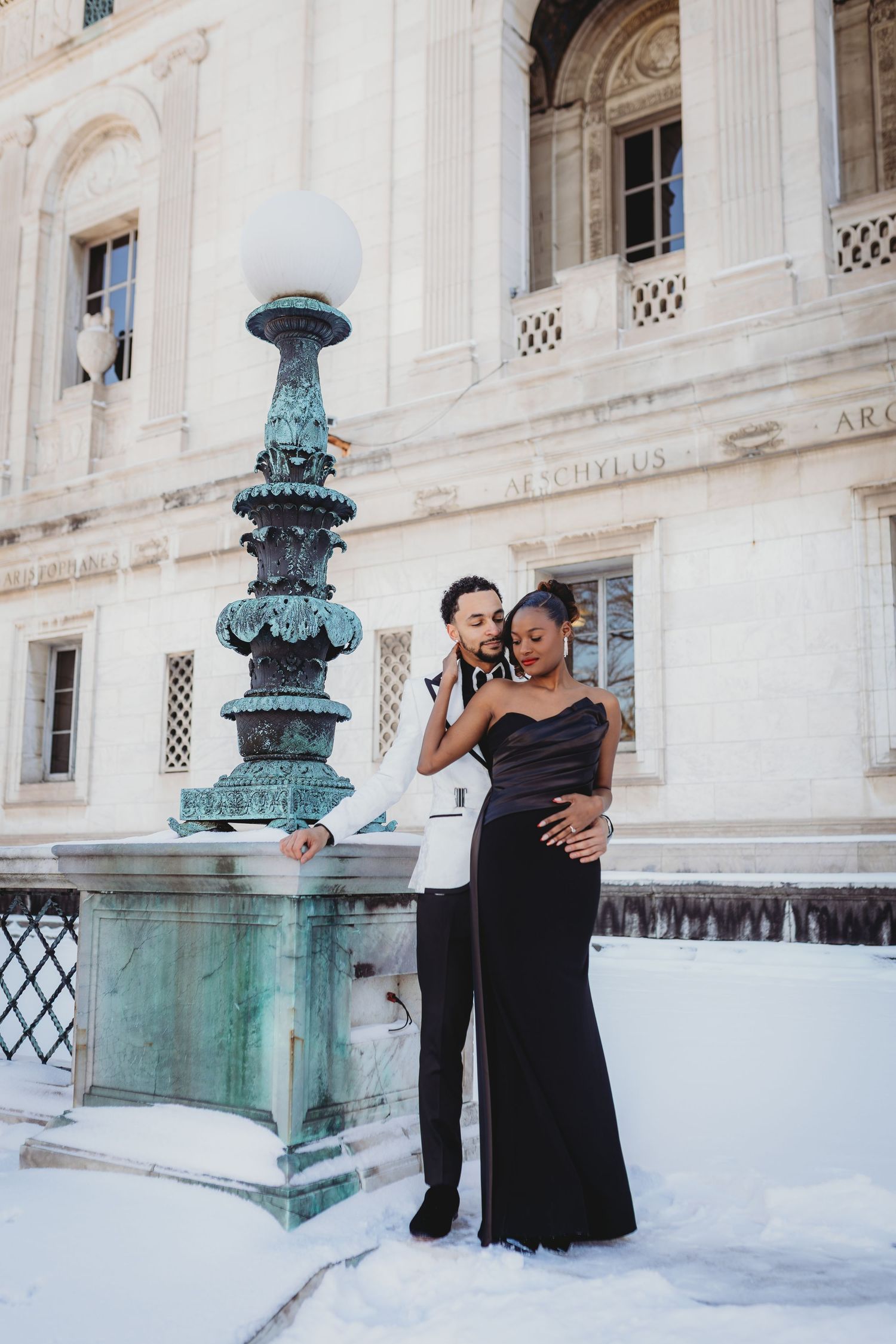A couple in formal attire shares an intimate dance moment against a grand architectural backdrop with ornate columns.