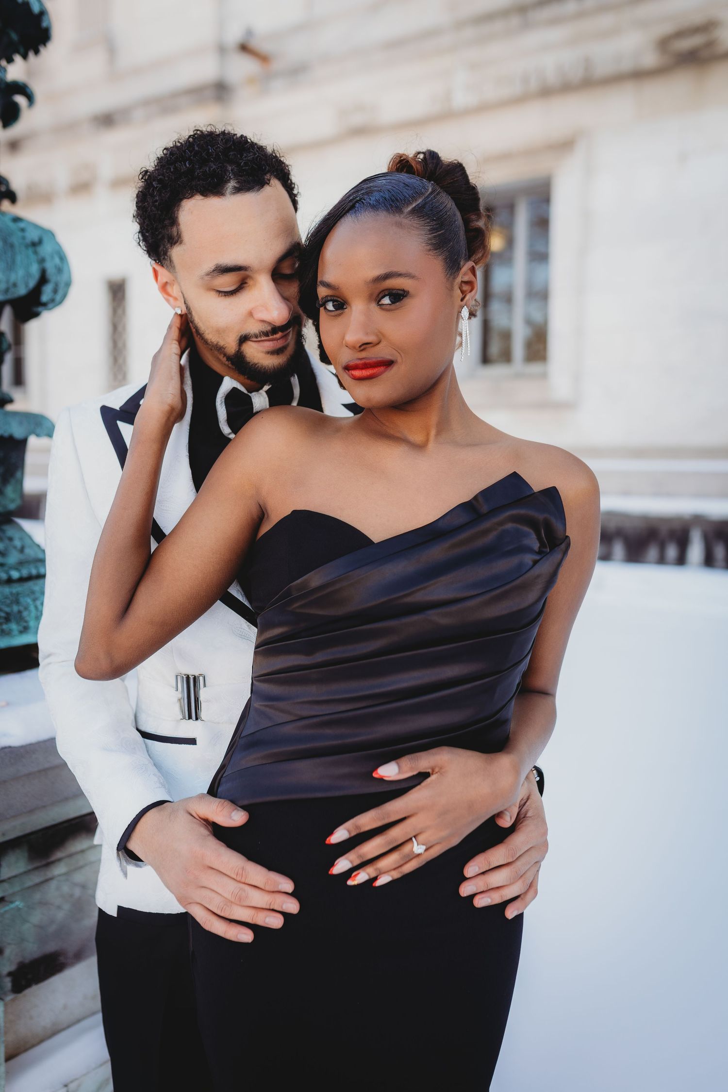 A romantic couple in black and white attire embraces tenderly during an outdoor photoshoot.