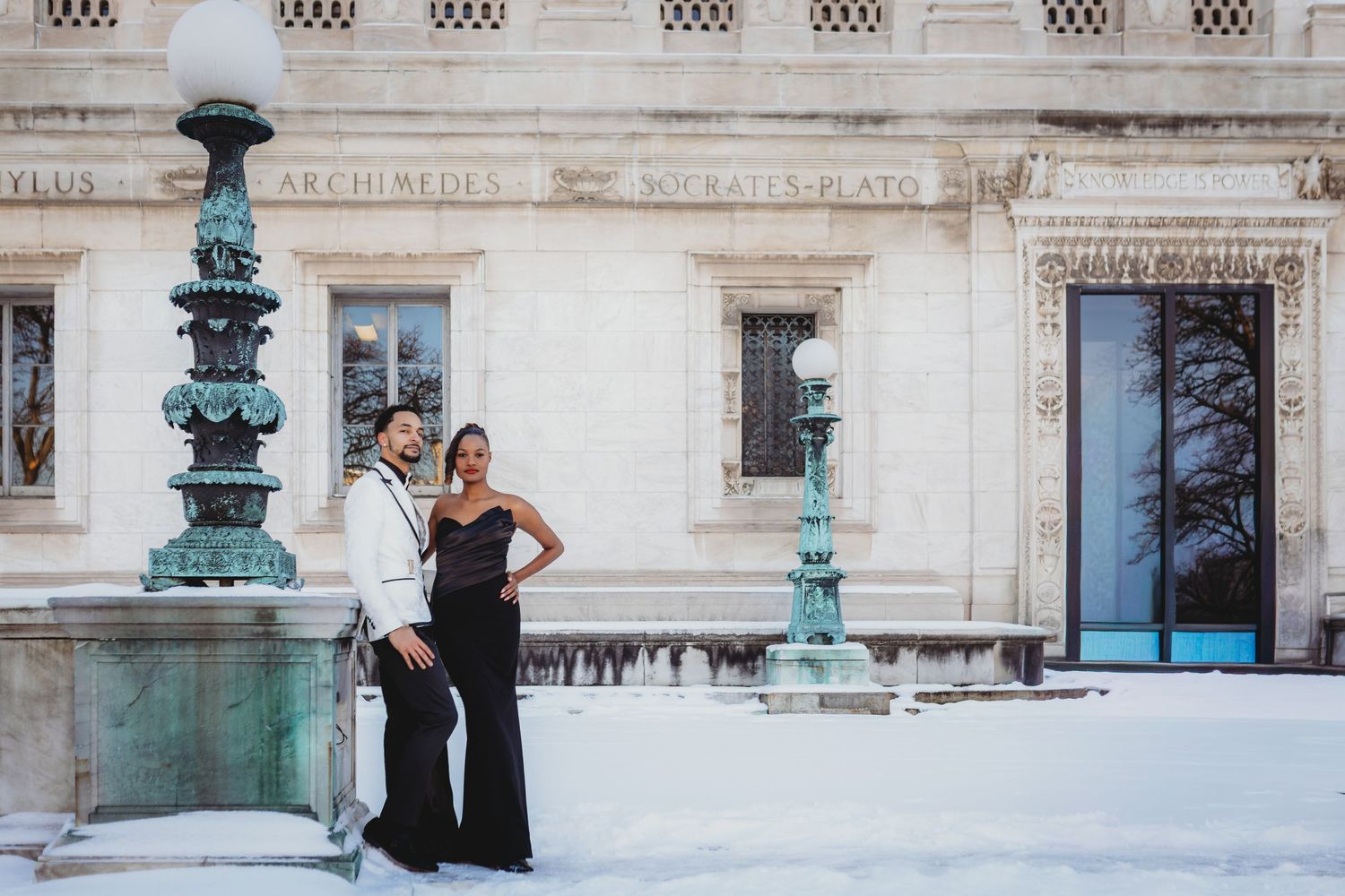 Elegant couple poses by ornate turquoise fountain outside historic building with classical architecture.