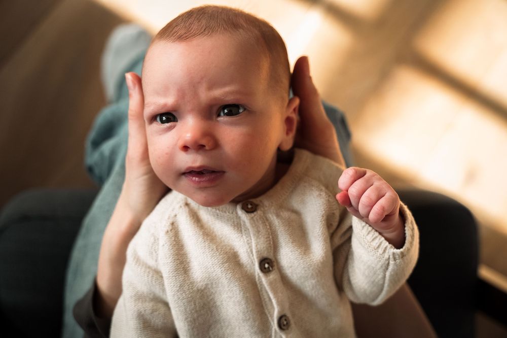 A baby in a cream colored sweater shows various expressions in a series of candid portrait shots.