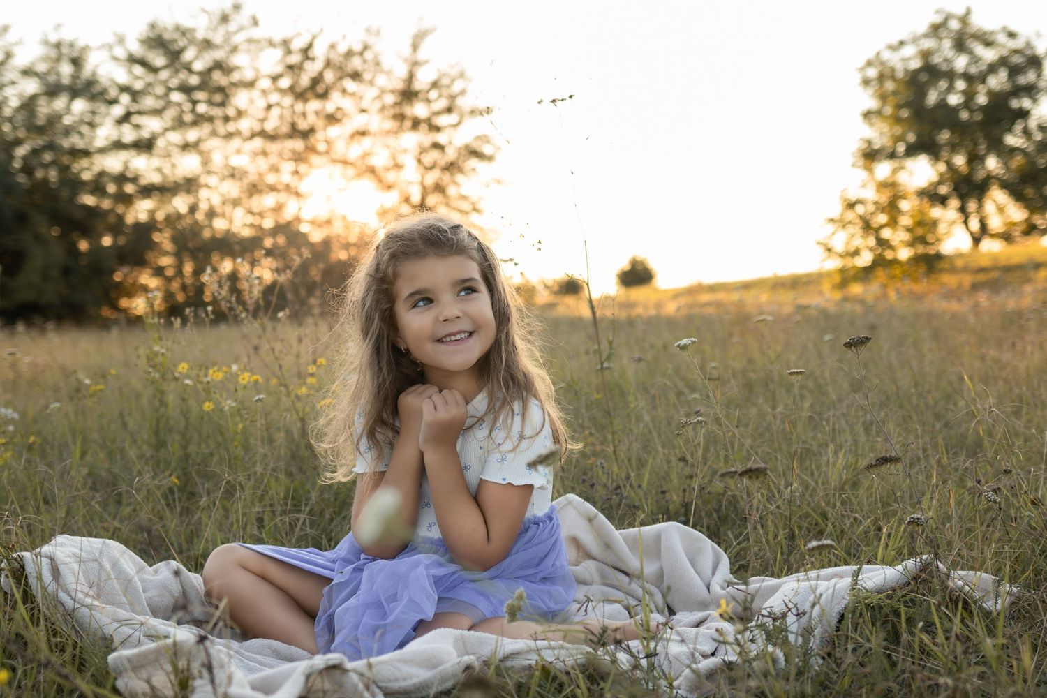 Young child sitting on blanket in field during golden hour sunset.