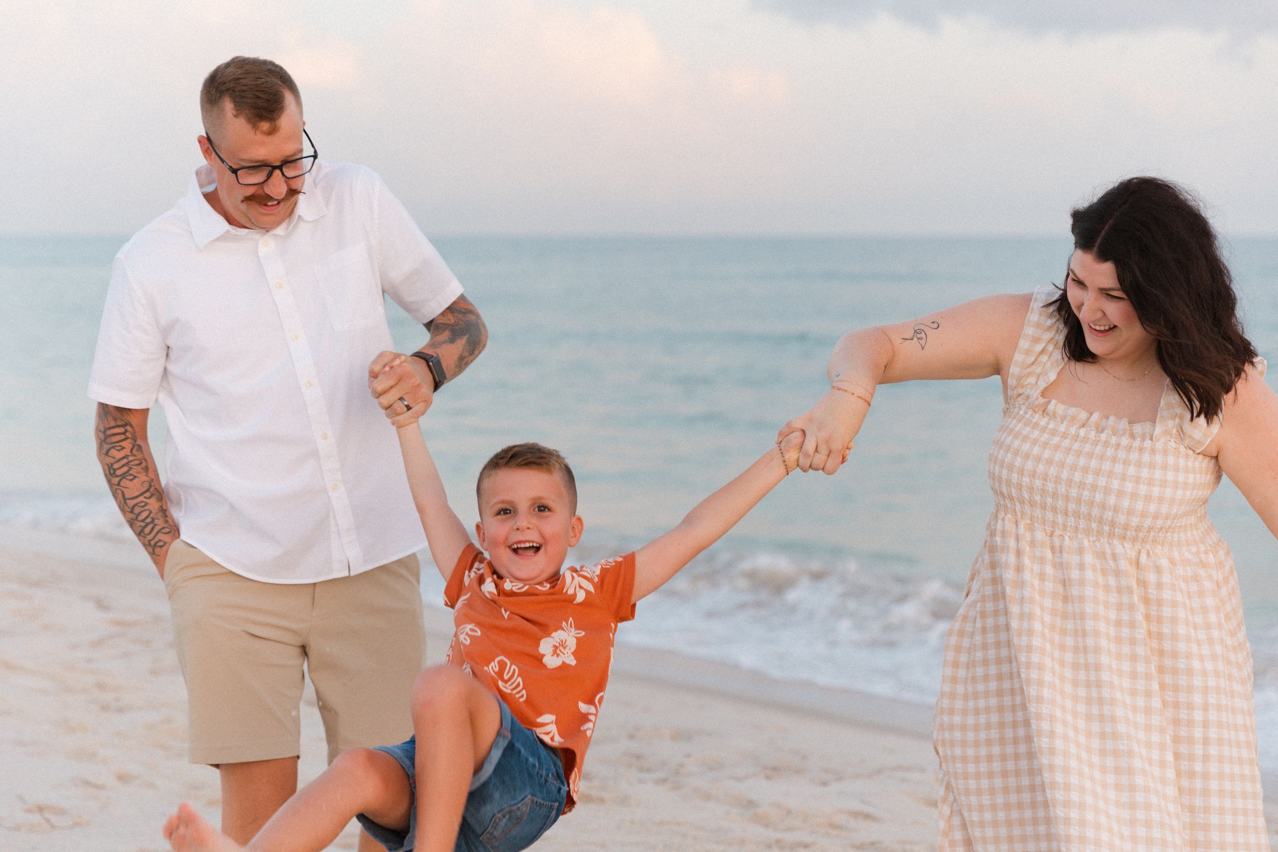 A family walks together along a sandy beach at sunset wearing coordinating beige and white outfits.