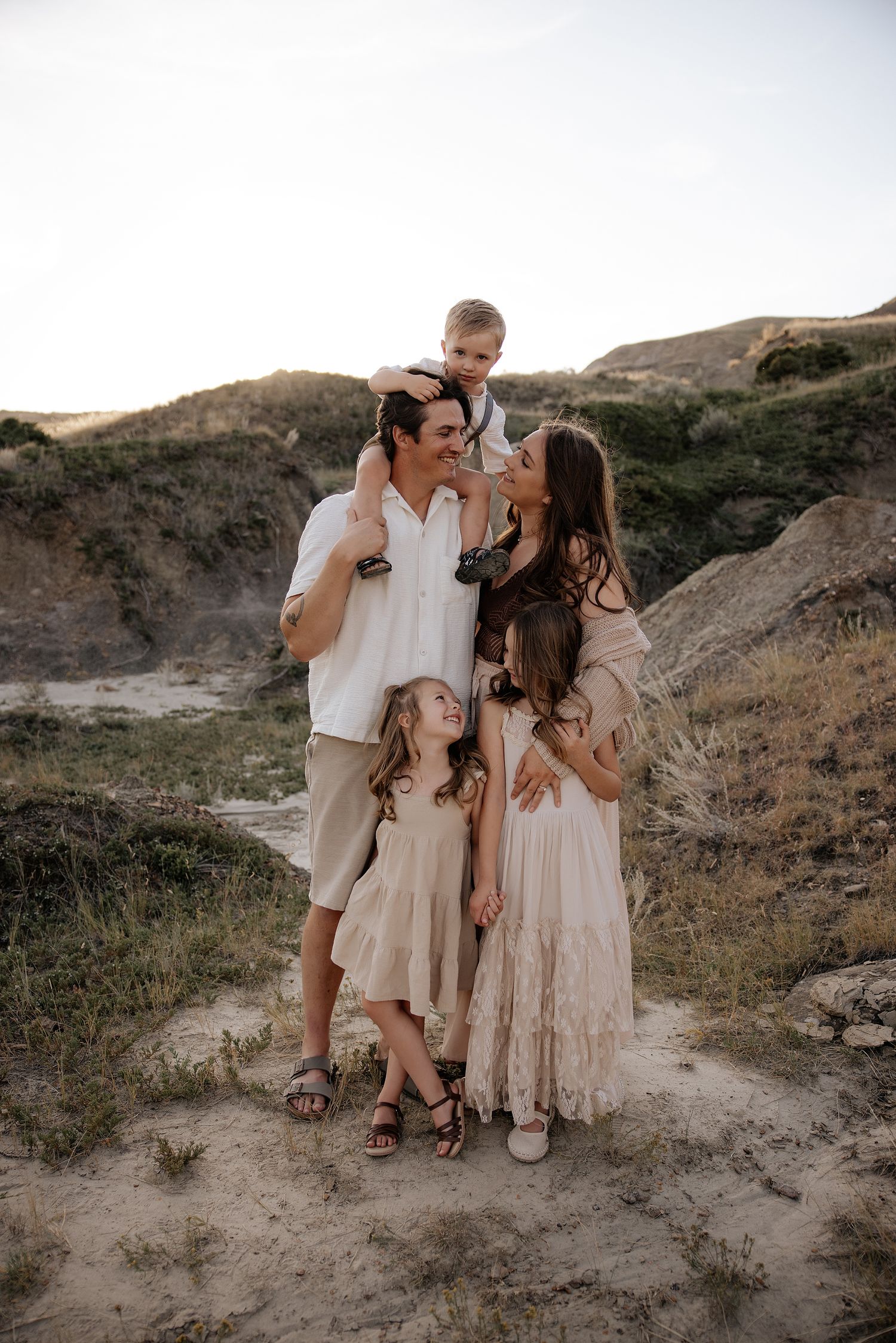 A family in neutral-toned outfits poses together on a rugged hillside during golden hour sunset.