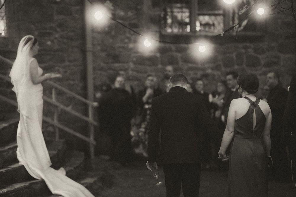 Black and white photos showing a wedding celebration with dancing guests and candid moments in a rustic venue.