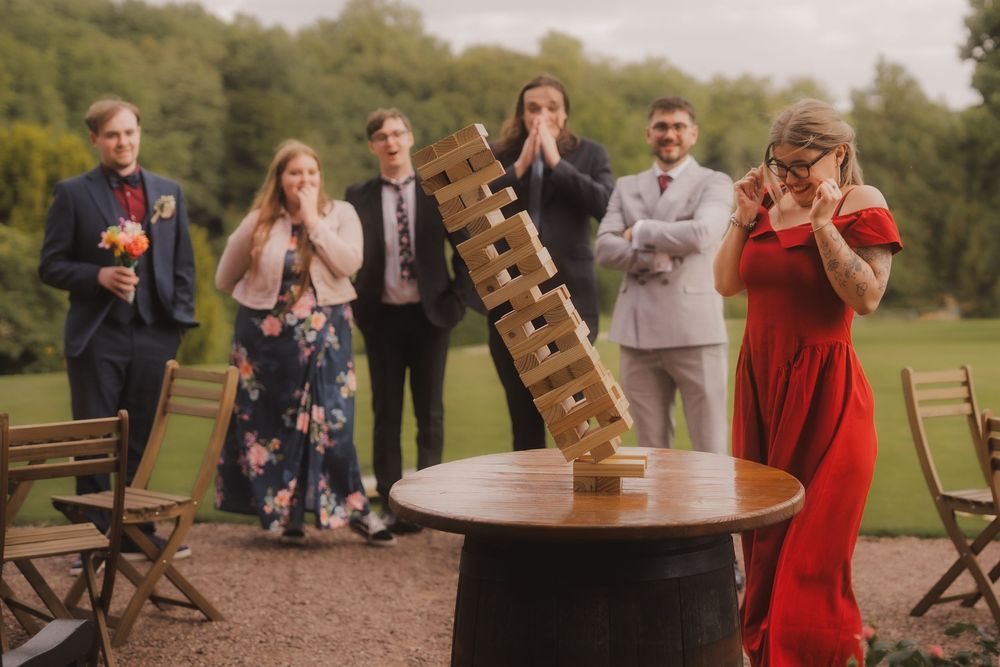 A group of people gather outdoors at a rustic wedding celebration with wooden folding chairs and natural scenery.
