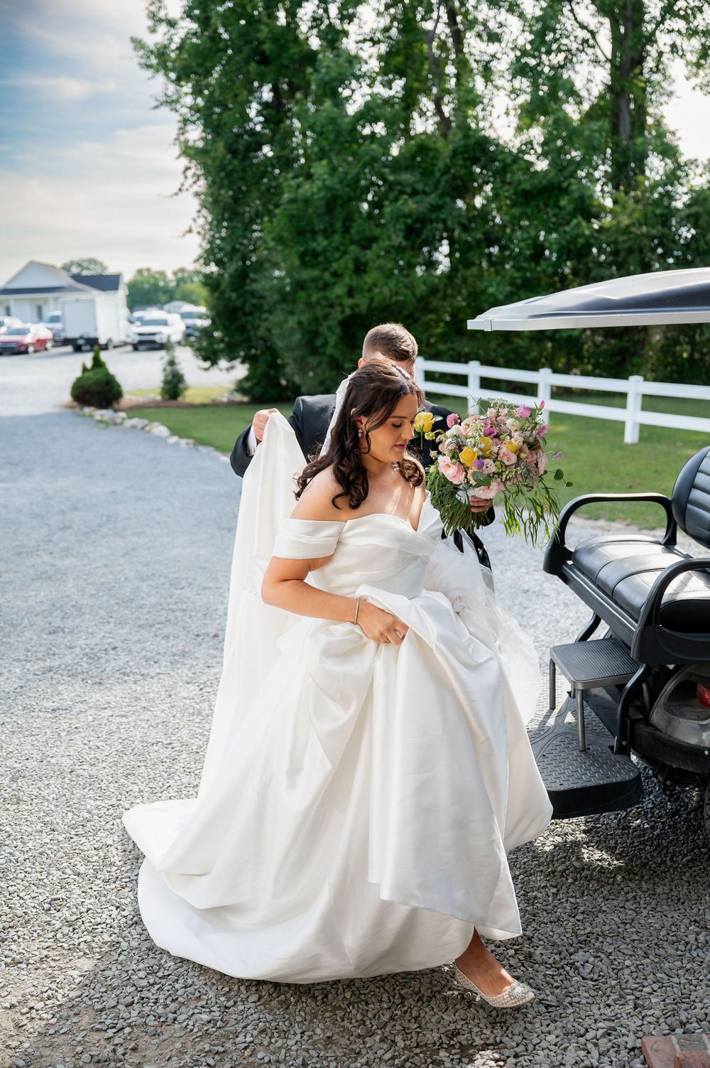 Wedding party in white dresses sitting together on gravel path.
