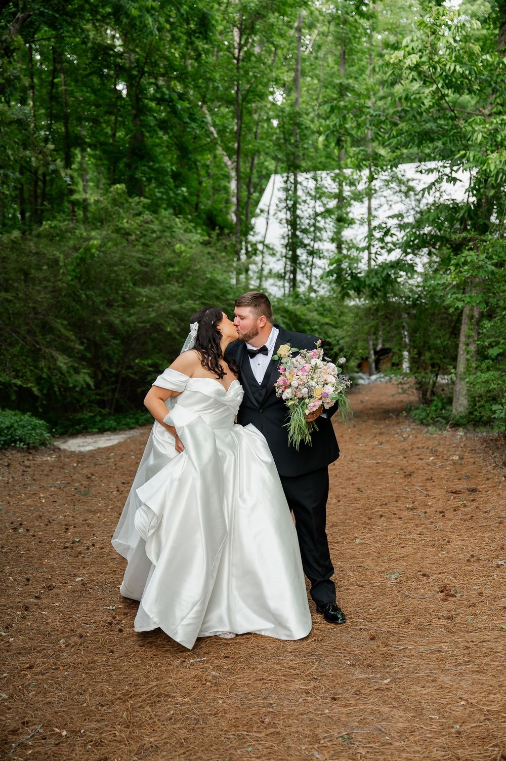 Wedding couple sharing romantic moment on forest path with flowing white dress.