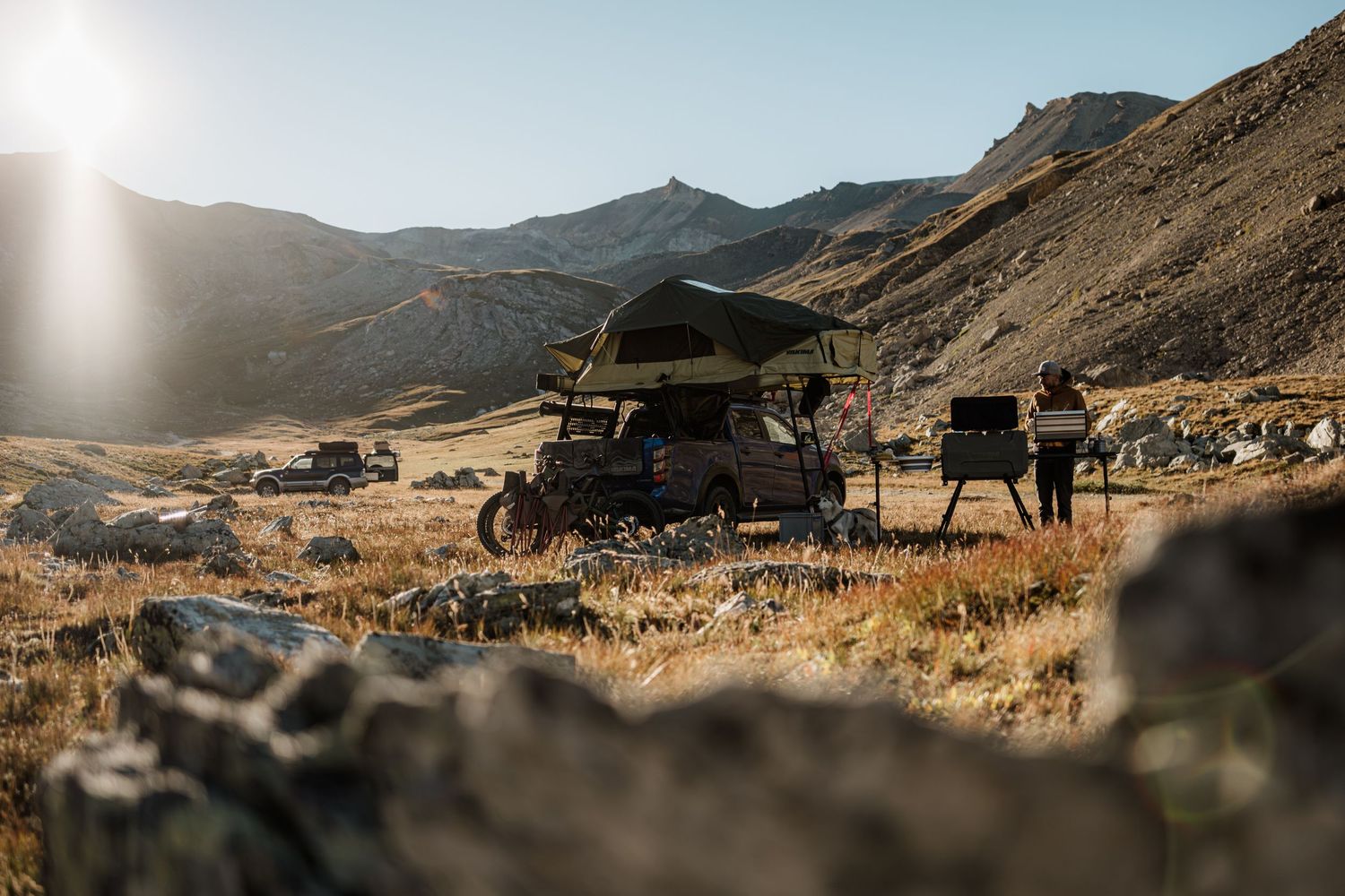 Panoramic view of a rugged mountain landscape with golden grass and dramatic sunlight filtering through the peaks.