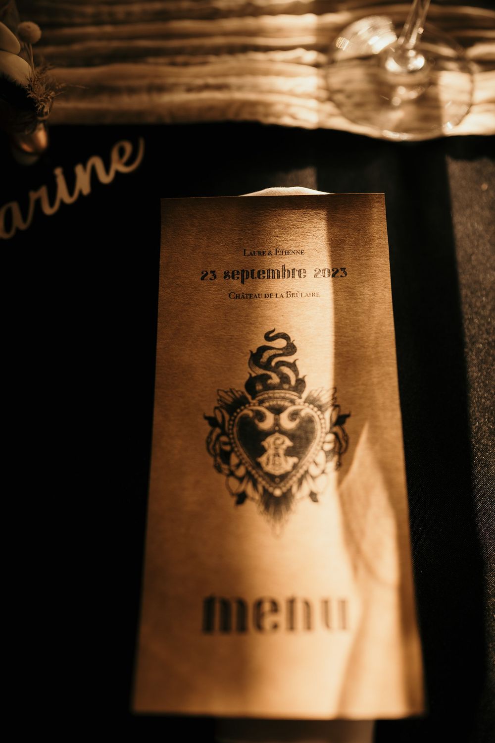 A vintage-style menu with an ornate crest design photographed in warm sepia tones on a wooden surface.