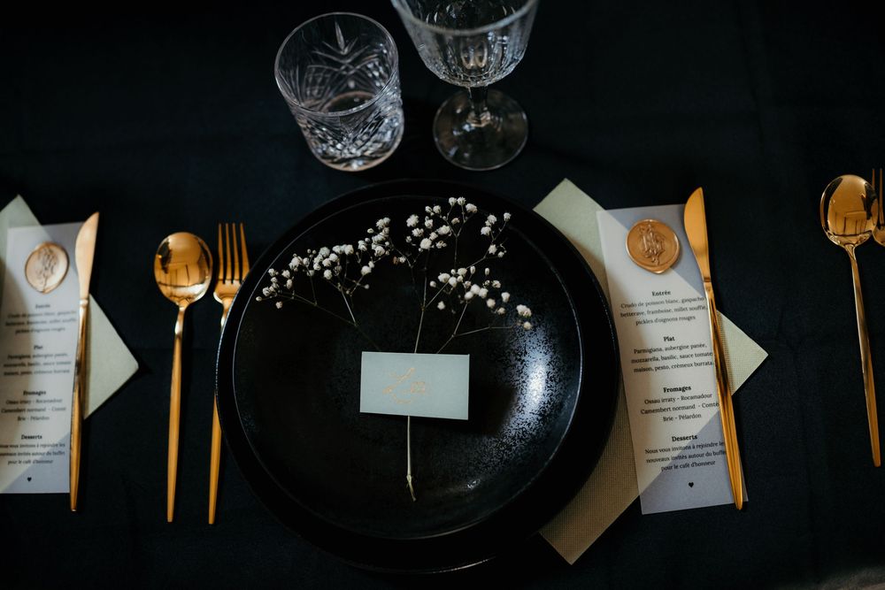 Elegant table setting with gold utensils, black plates, and menu cards arranged on a dark surface.