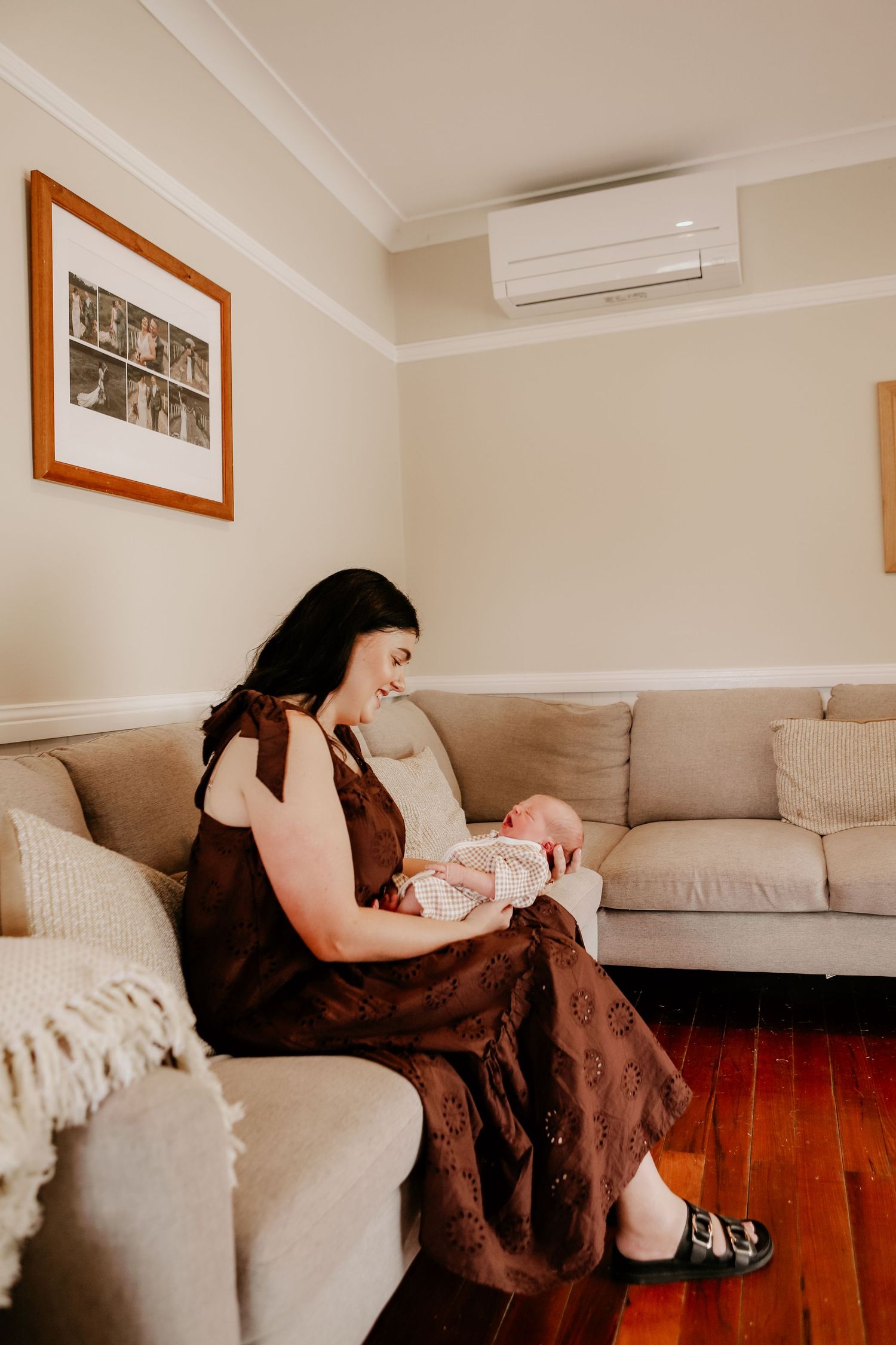 A person in a brown dress rests on a beige couch in a modern living room with hardwood floors and framed artwork.