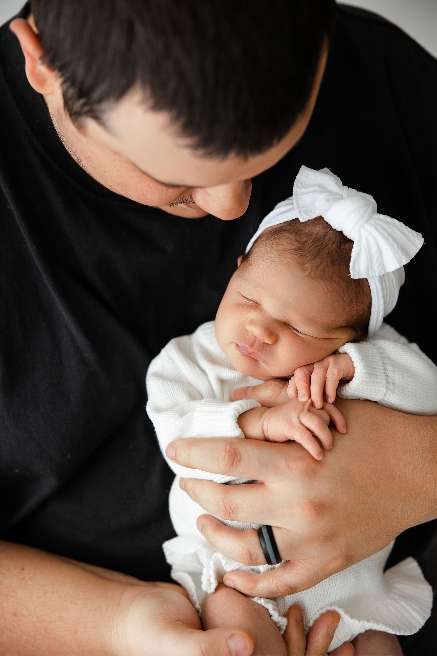 Series of black and white photos capturing a parent cradling and bonding with their sleeping newborn baby.