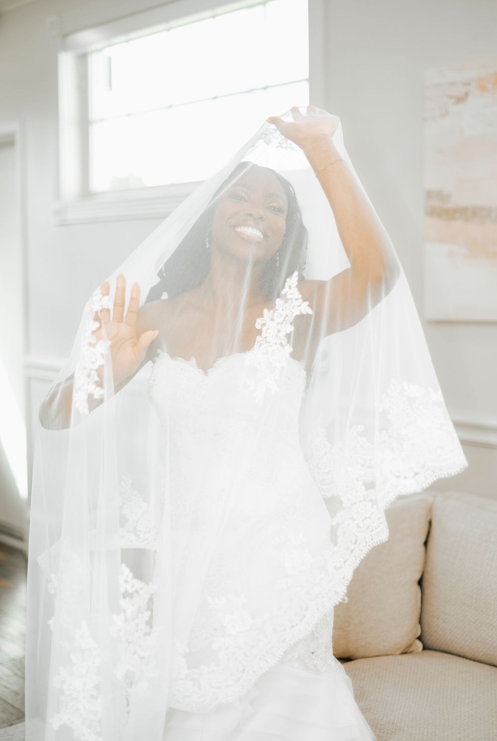 A delicate white lace veil with intricate floral patterns flows elegantly in natural light against a bright interior setting.