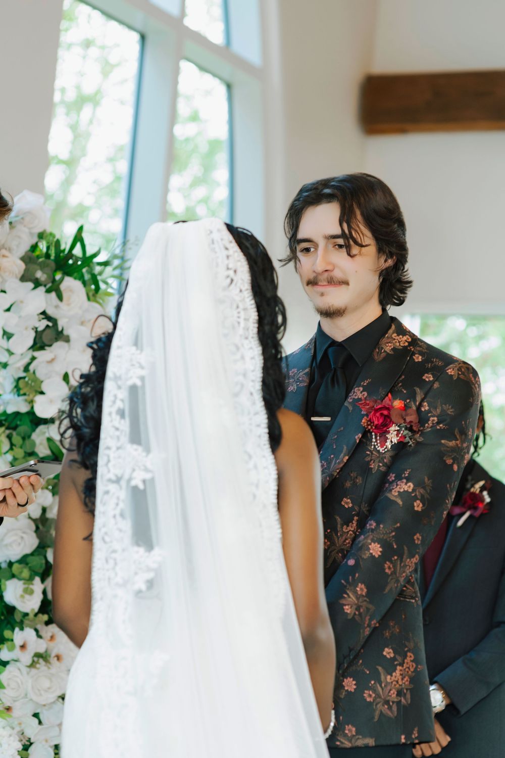 A couple shares an intimate moment during their wedding ceremony surrounded by white floral decorations.