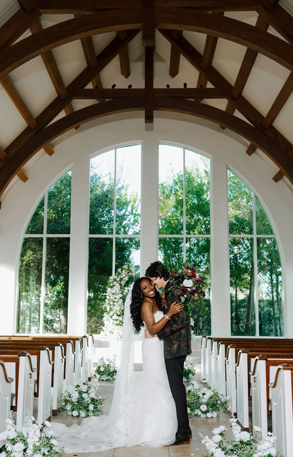 A romantic wedding ceremony scene in an elegant white arched colonnade decorated with floral arrangements.