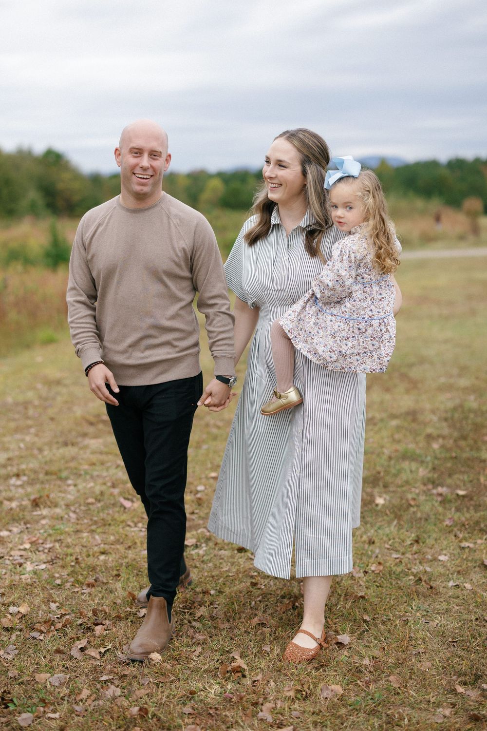 A family walking together through a grassy field on an overcast autumn day.