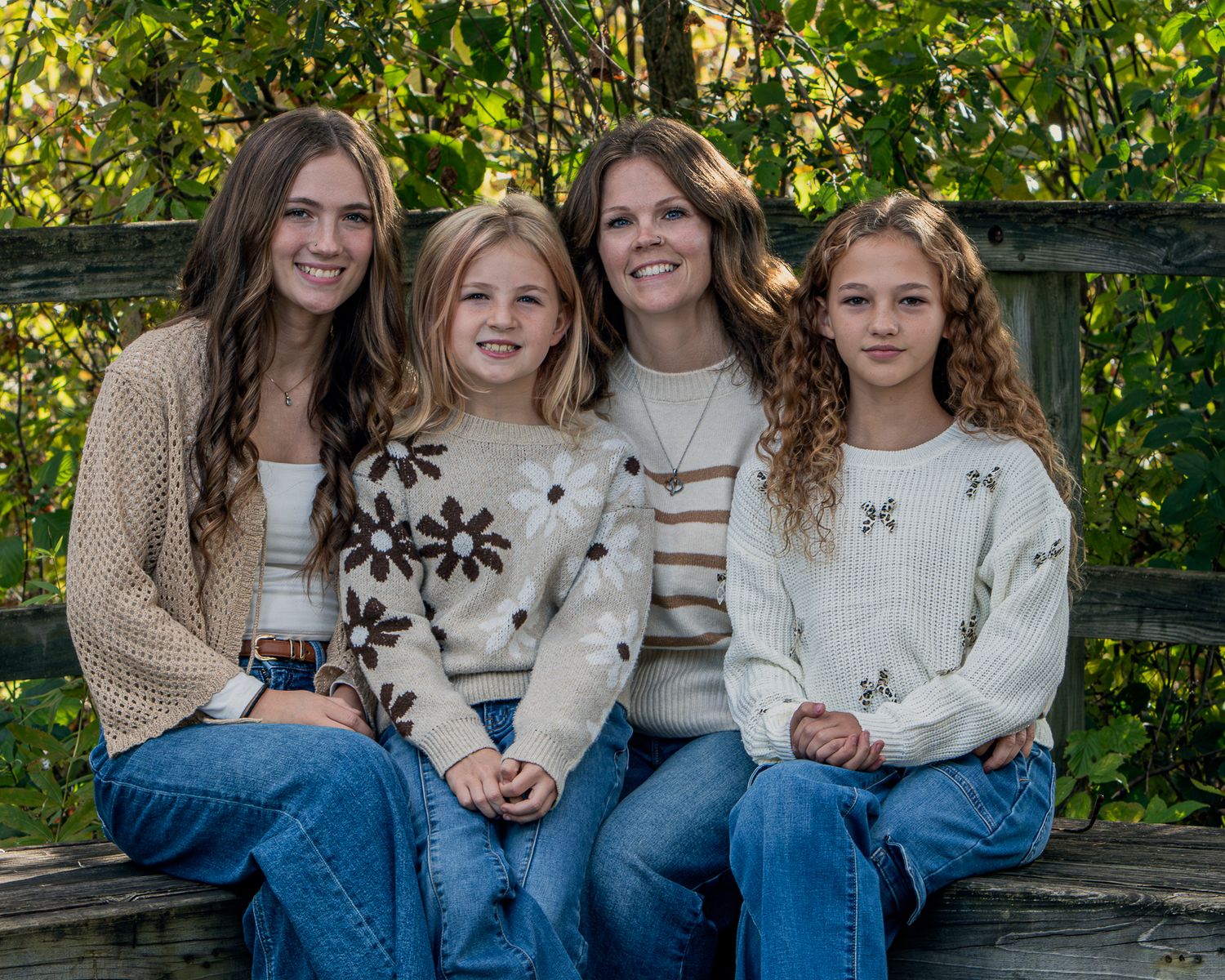 A group in coordinated cream sweaters and blue jeans sits together on wooden steps outdoors in a natural setting.