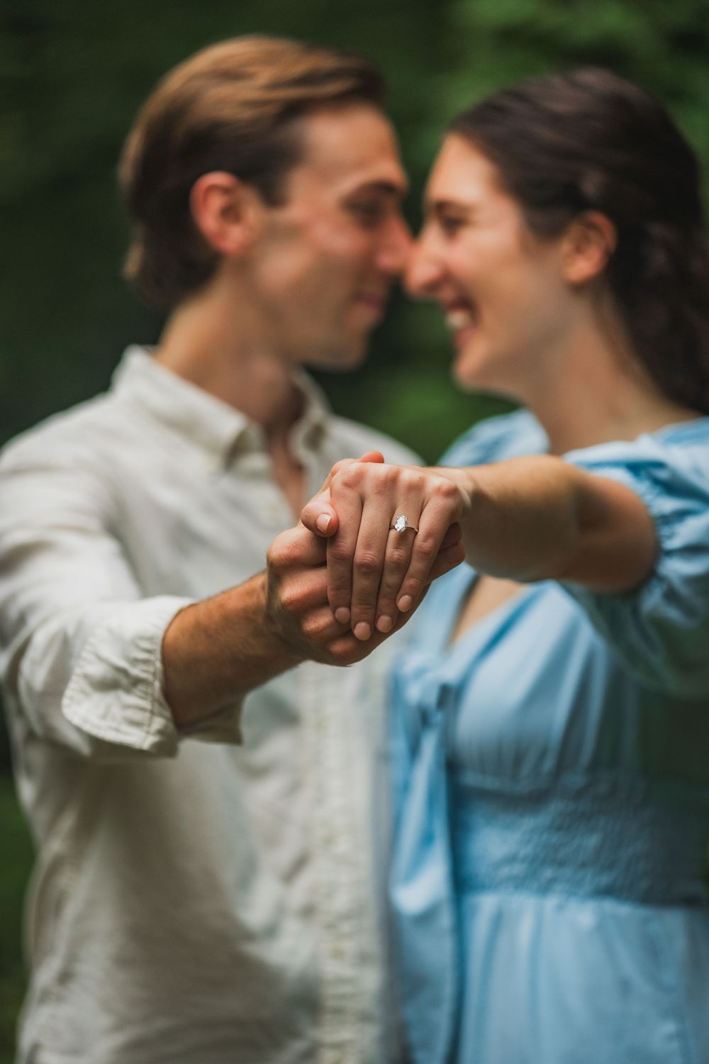 A romantic couple holding hands and laughing together in a candid outdoor moment with soft focus on the new engagement ring