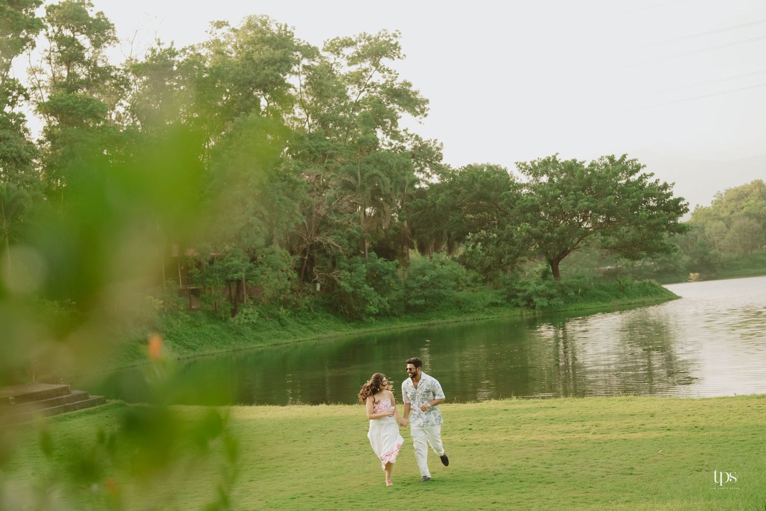 A distant view of a couple walking along a peaceful lakeside path surrounded by lush greenery.