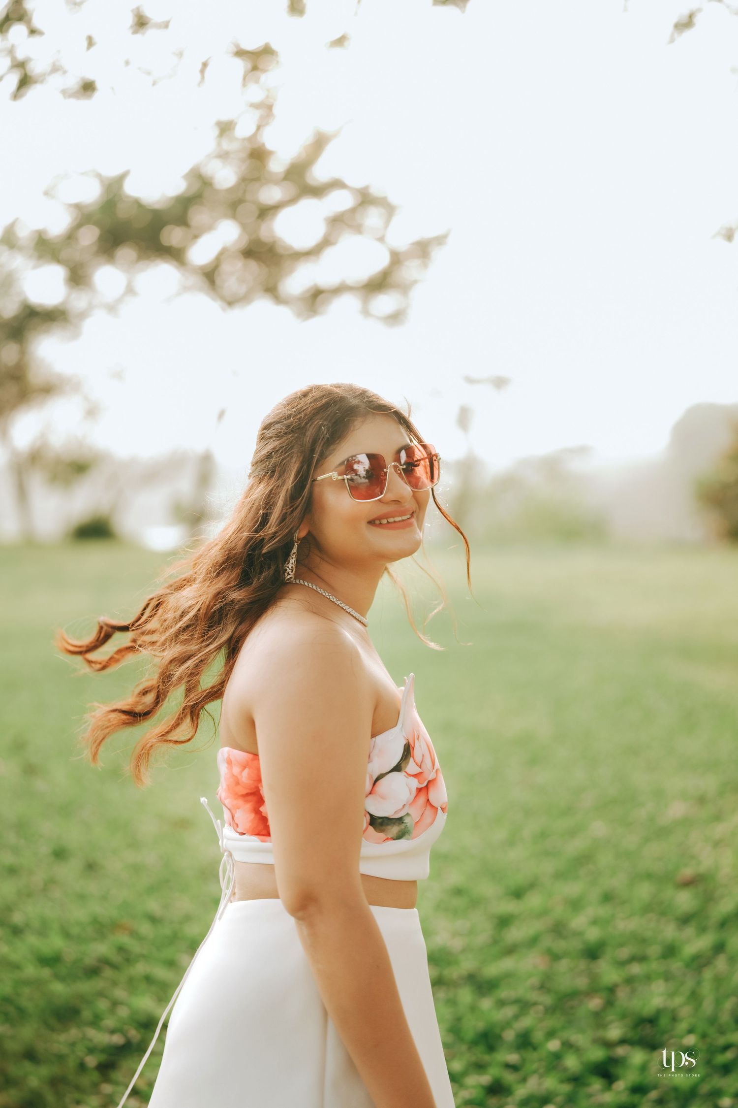 A portrait of someone in a white floral dress and red sunglasses enjoying a sunny day outdoors.