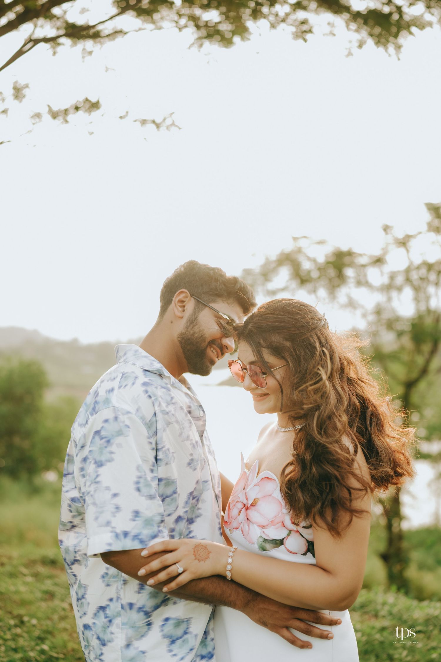 A couple embraces while dancing in a sunlit field with trees in the background.