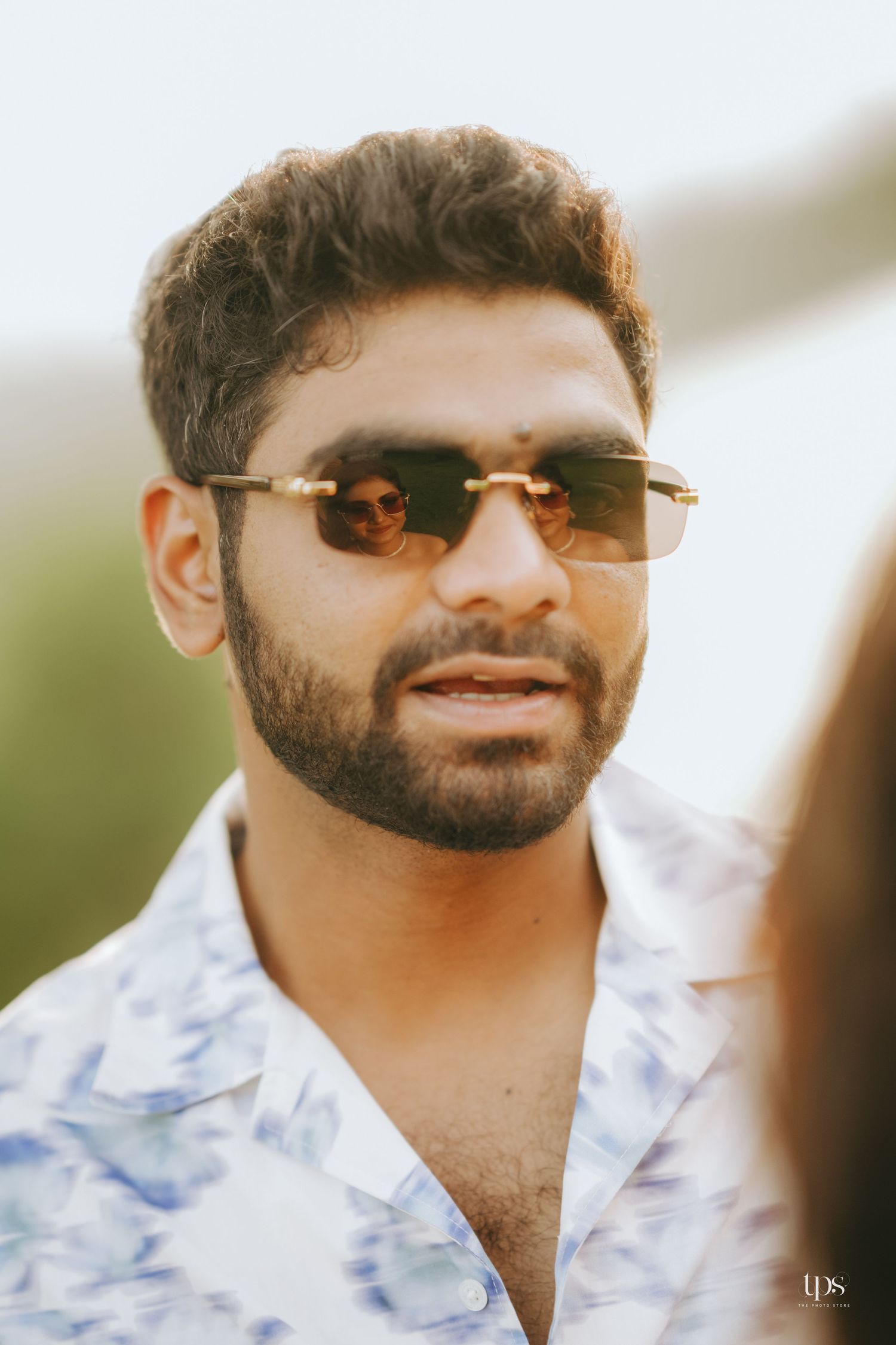 Close-up profile shot of someone wearing sunglasses and a blue patterned shirt.