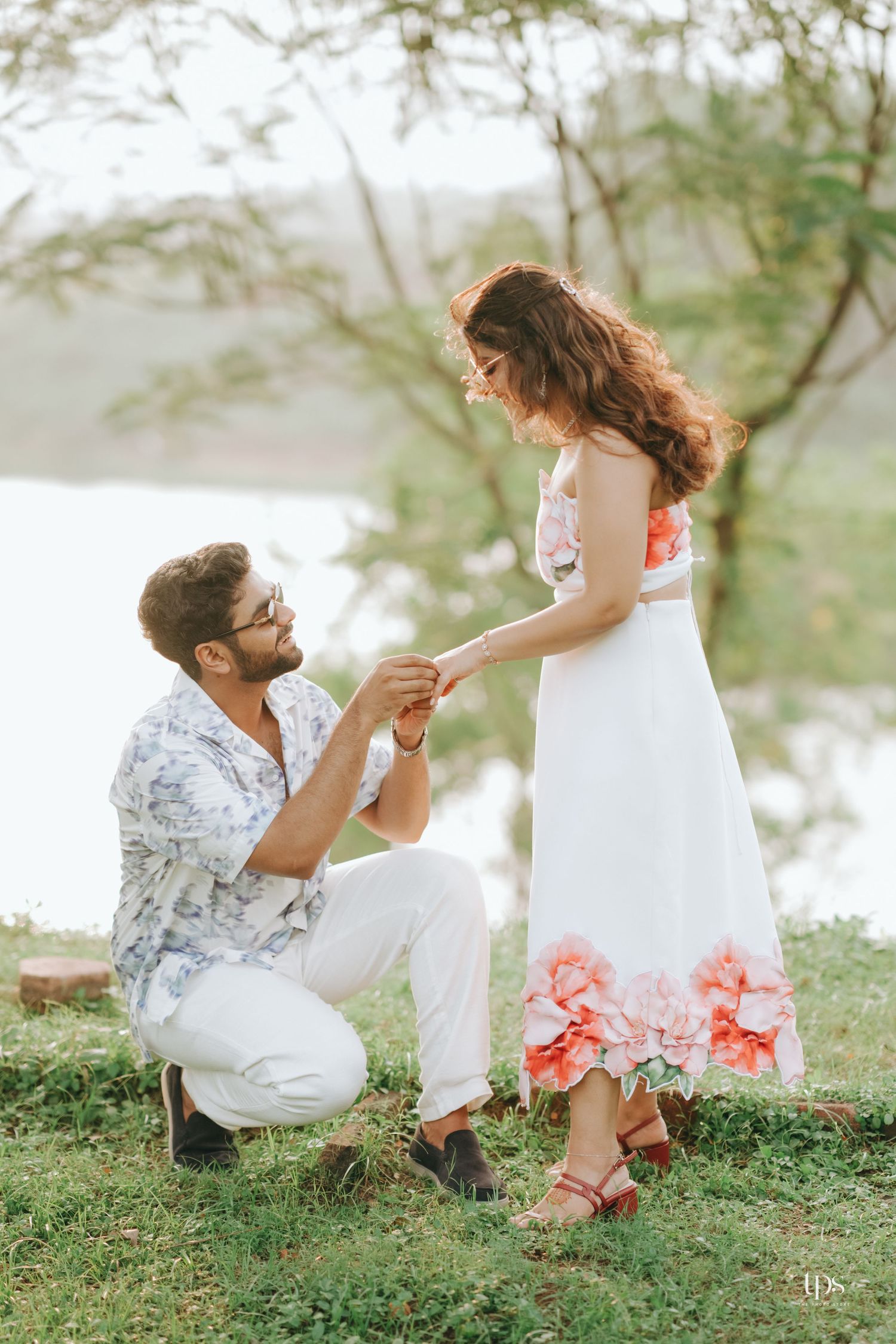 Romantic outdoor photoshoot featuring a couple sitting on grass with pink flowers and soft lighting.