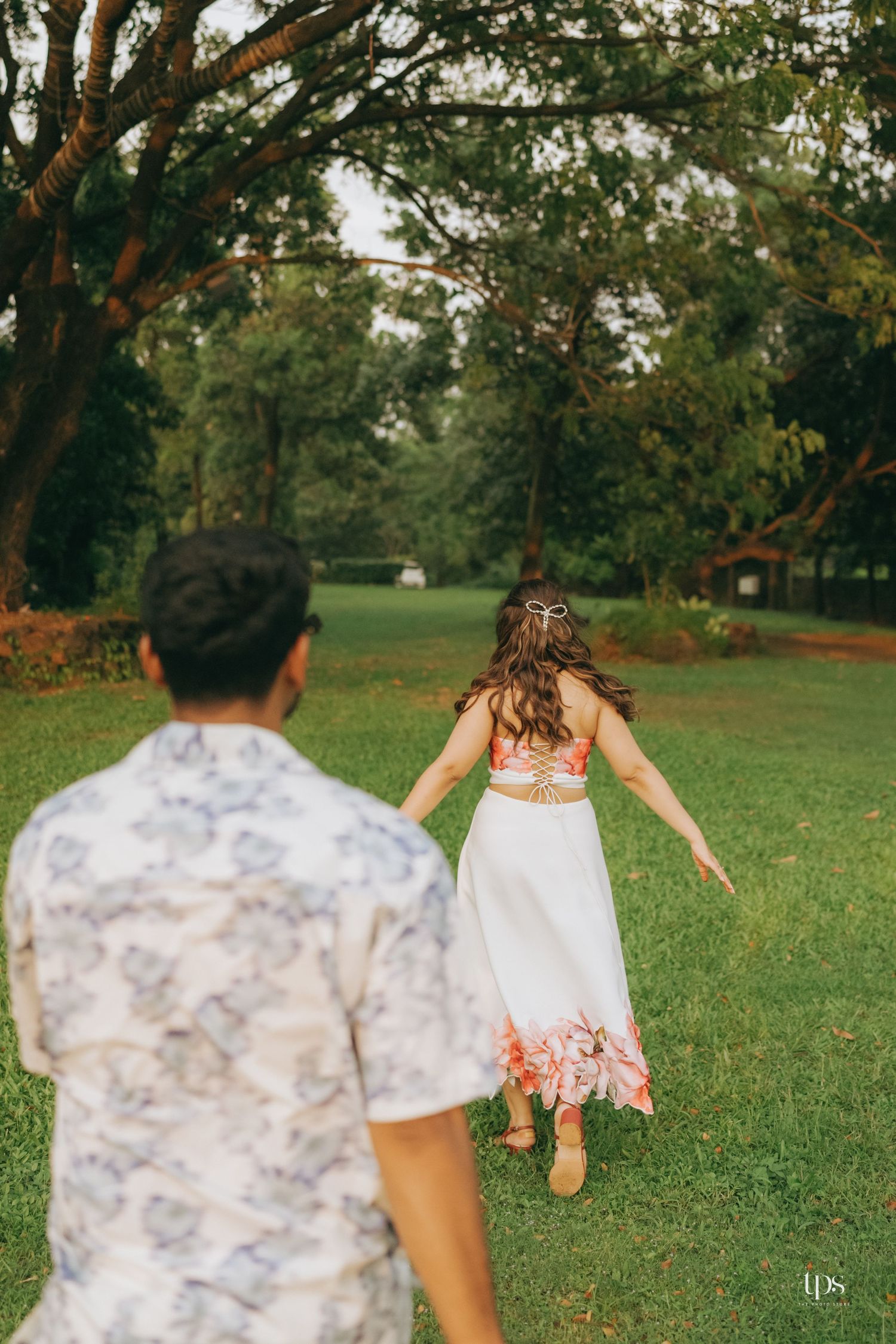 Playful couple running through a green park wearing coordinated white and floral outfits.