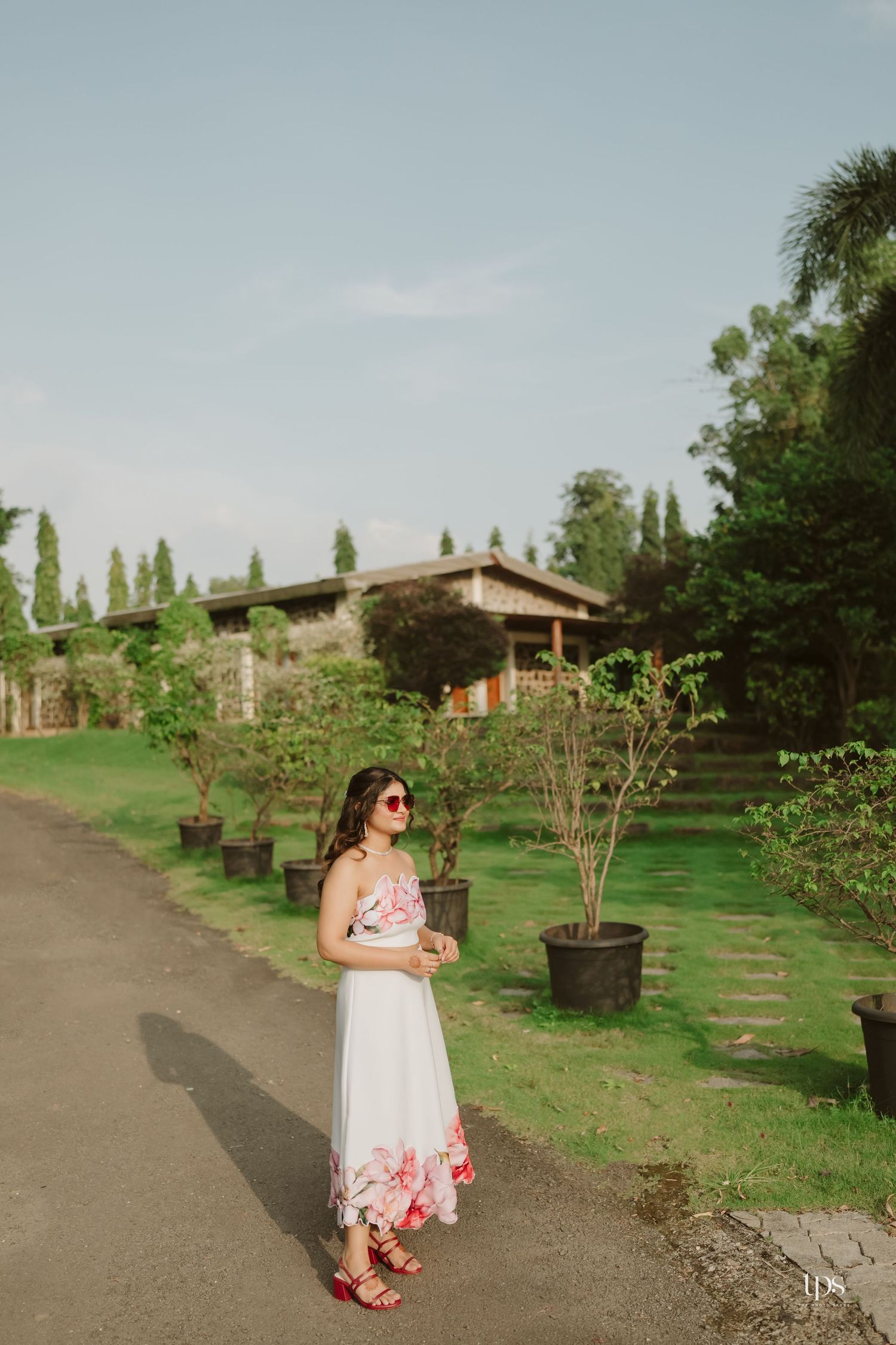 A white sundress with pink floral details photographed against a rustic stone building and garden.