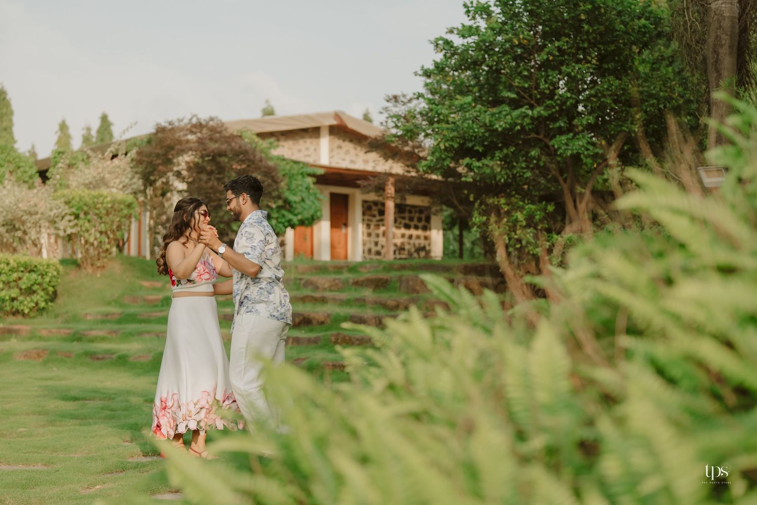A romantic moment captured in a lush garden setting with a stone building backdrop.