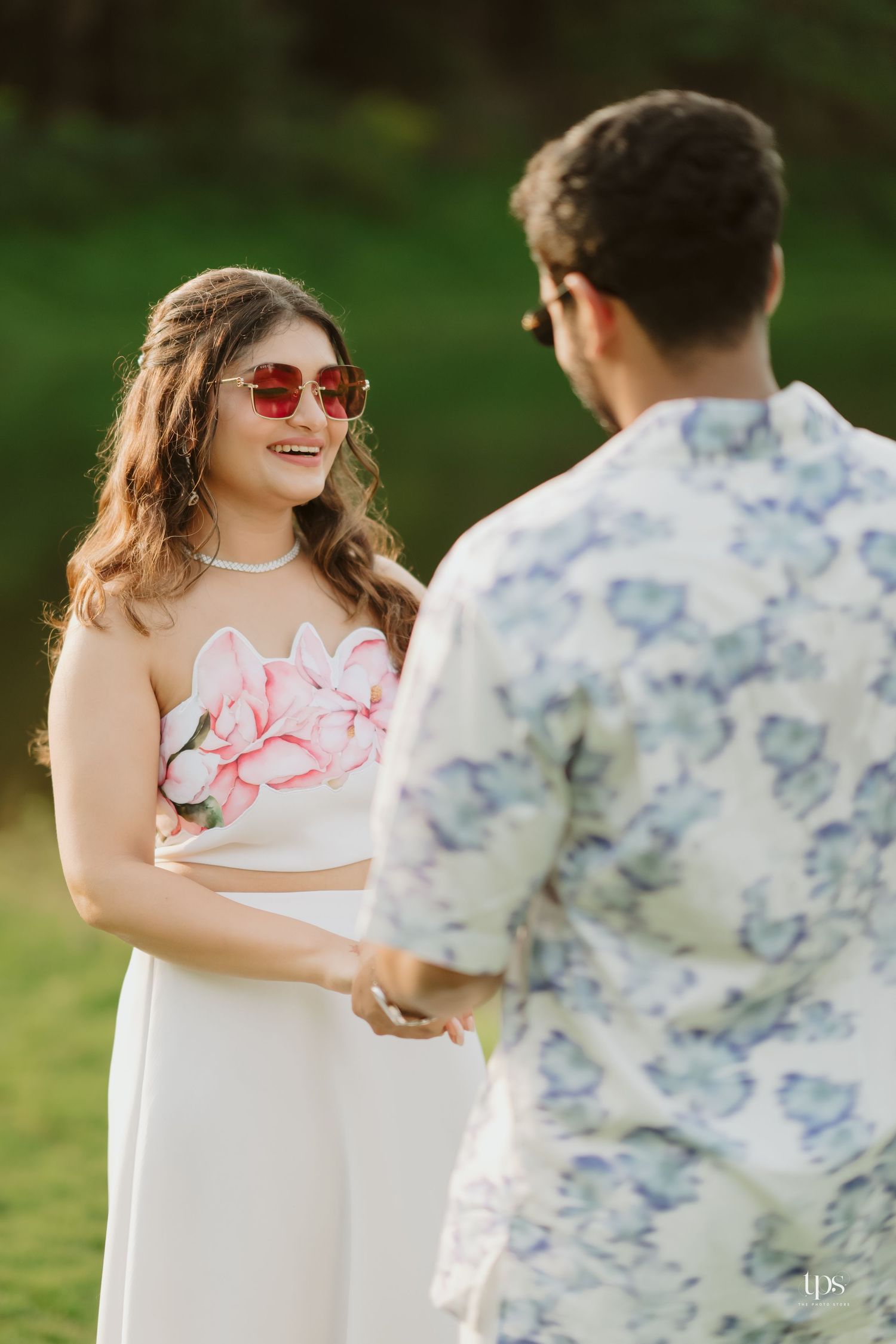 A couple in coordinated outfits sharing a romantic moment by a lake, with her in a floral dress and him in a floral shirt.
