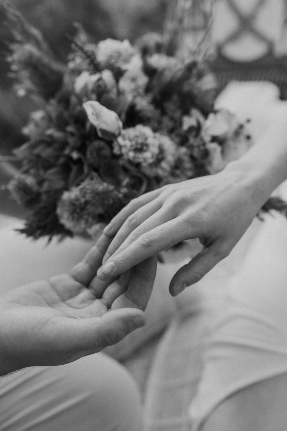 Close-up of two hands touching tenderly with blurred flowers in the background.