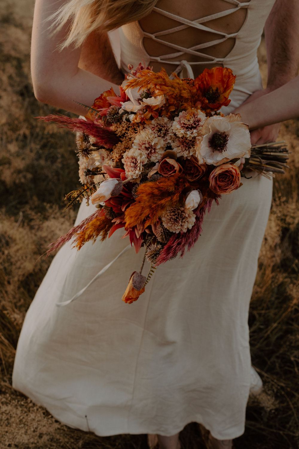 White dress with lace-up back detail holding vibrant autumn-colored wedding bouquet.