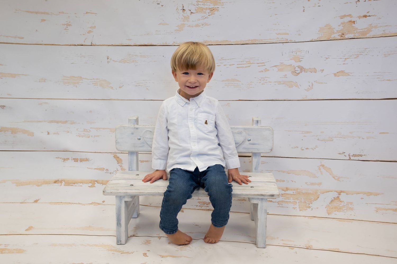 young boy smiling on a white bench in a studio