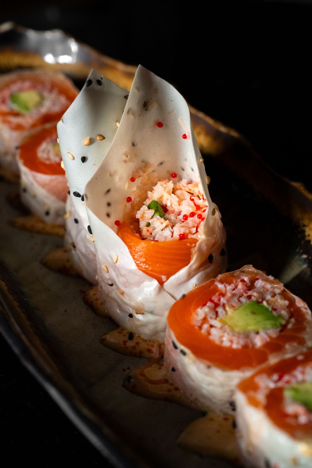 Beautifully arranged sushi rolls with salmon and garnishes on dark plate with dramatic lighting. Mtlshutter photography
