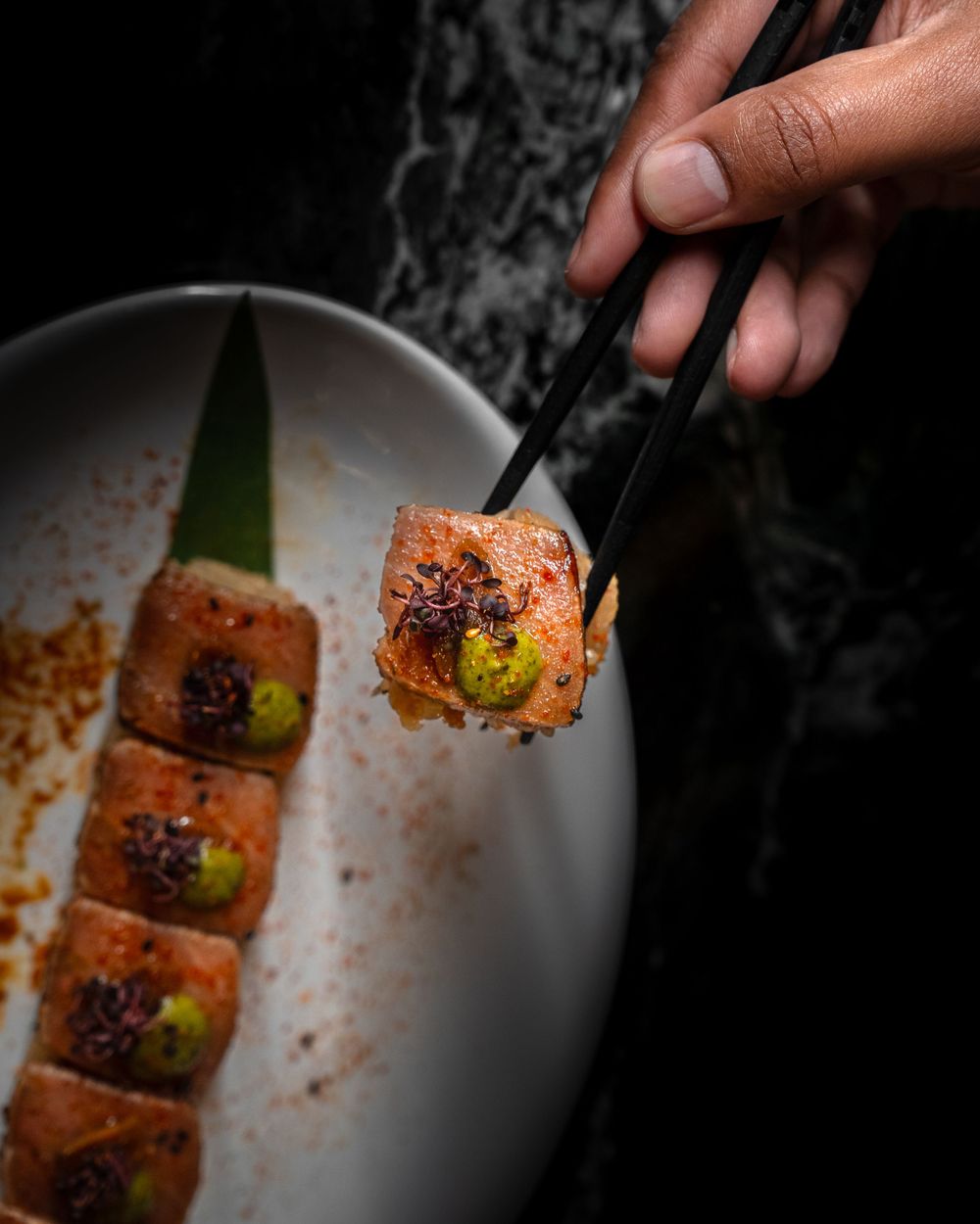 Close-up of seared sushi roll being picked up with chopsticks against dark background. Mtlshutter photography