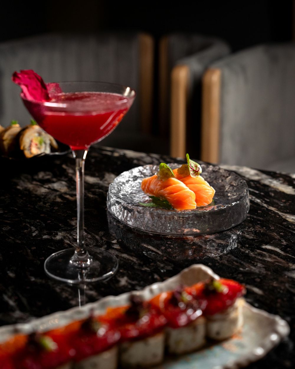 Vibrant red cocktail and fresh sashimi served on black marble surface with artistic presentation. Mtlshutter photography