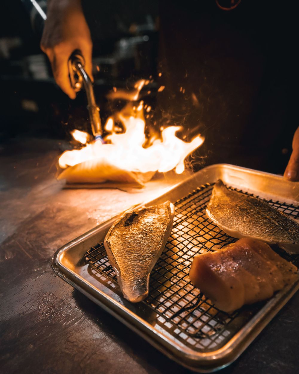 Dramatic flambé cooking of meat on a metal grill rack with flames. Mtlshutter photography
