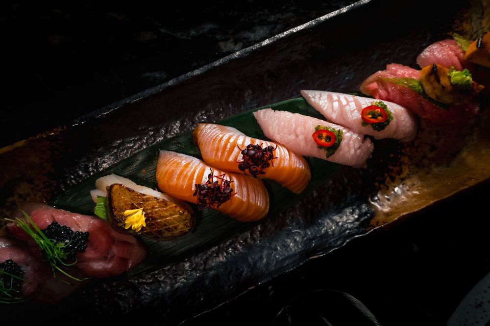 Artistically plated nigiri sushi selection on long black stone plate with dramatic lighting. Mtlshutter photography
