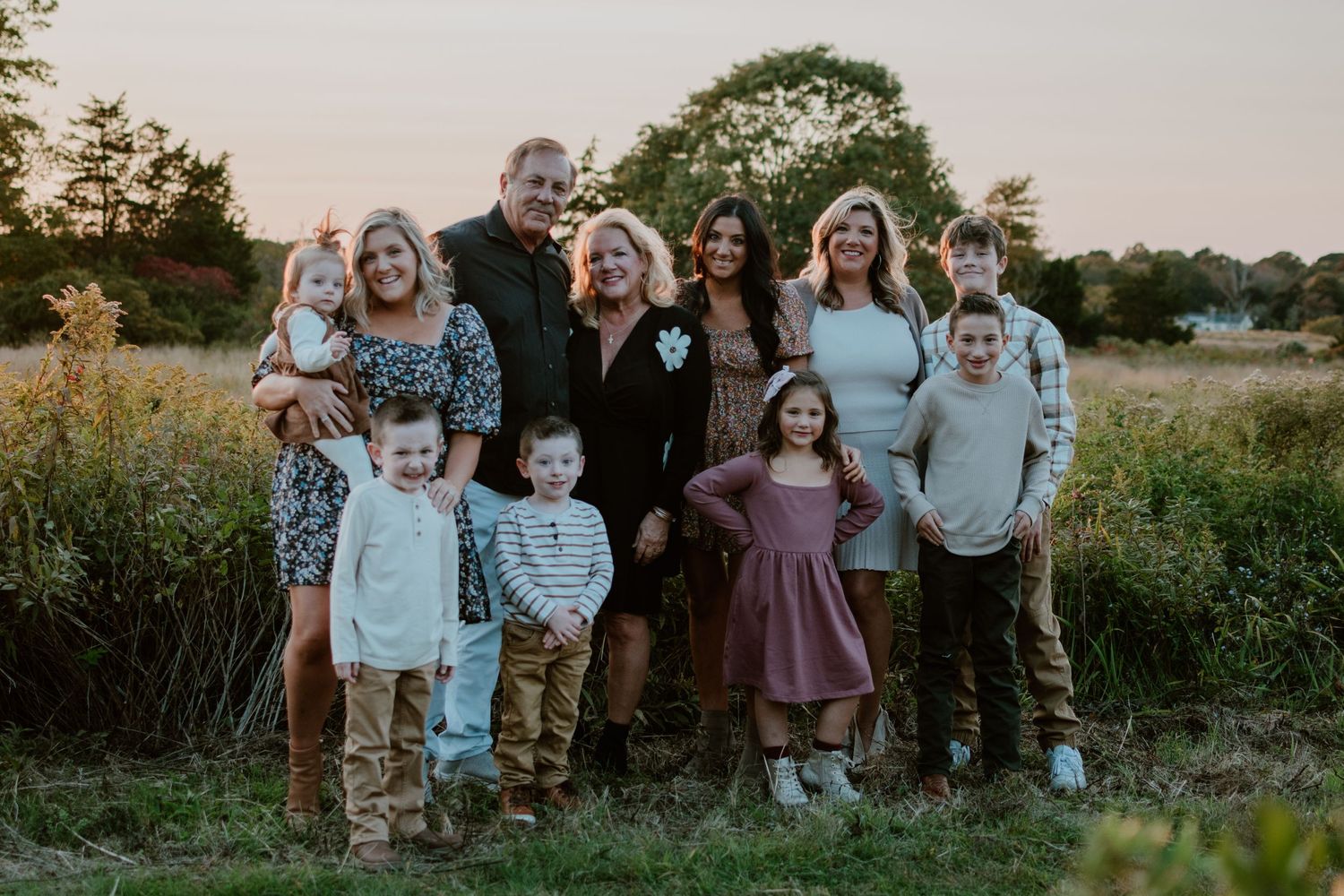 A group of ten people in coordinating outfits pose together outdoors at sunset in a grassy field.