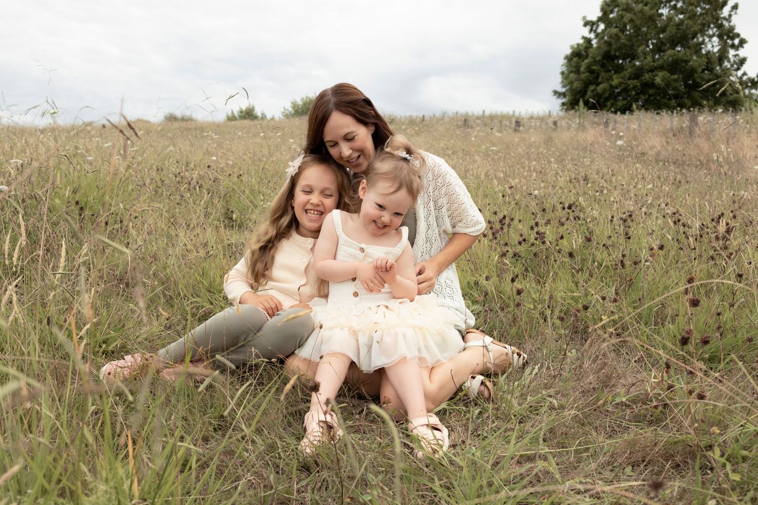 A tender moment shared in a tall grass field on a bright summer day as three people embrace and smile together.