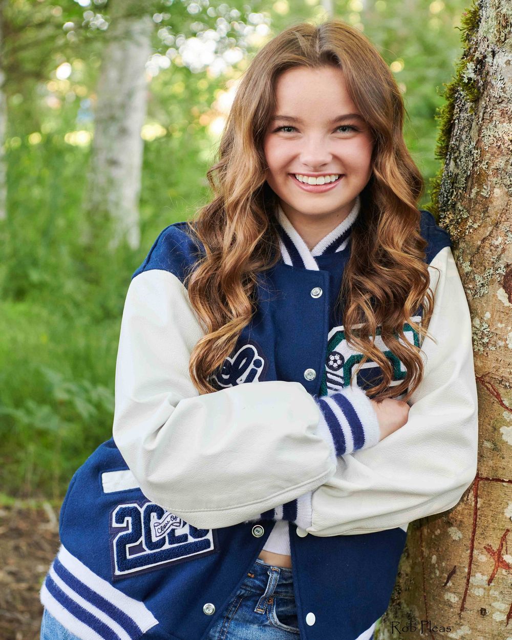 High school senior wearing blue and white Letterman's jacket while leaning against tree at Decoursey Pond in Puyallup, WA