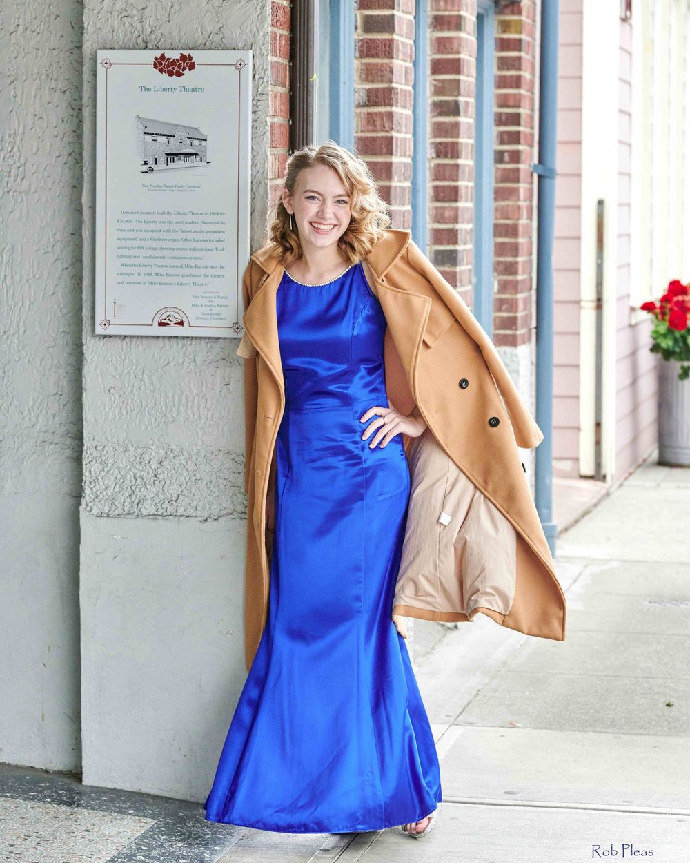 High school senior female wearing blue dress while wind blows tan jacket open at Liberty Theatre in Puyallup, WA